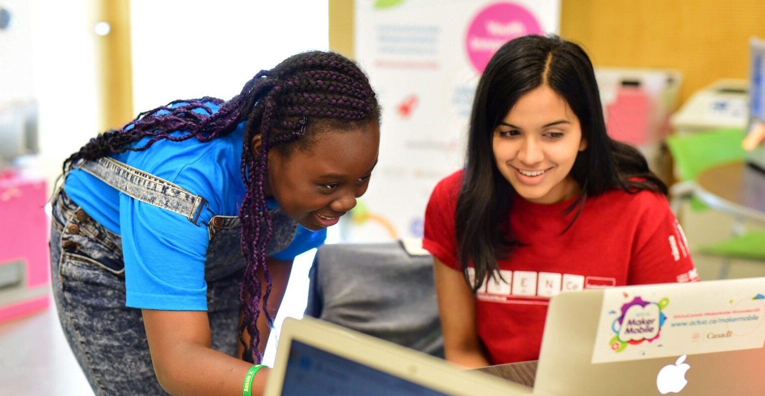 Two young females looking at something on the computer to demonstrate the interactivity of the workshops.