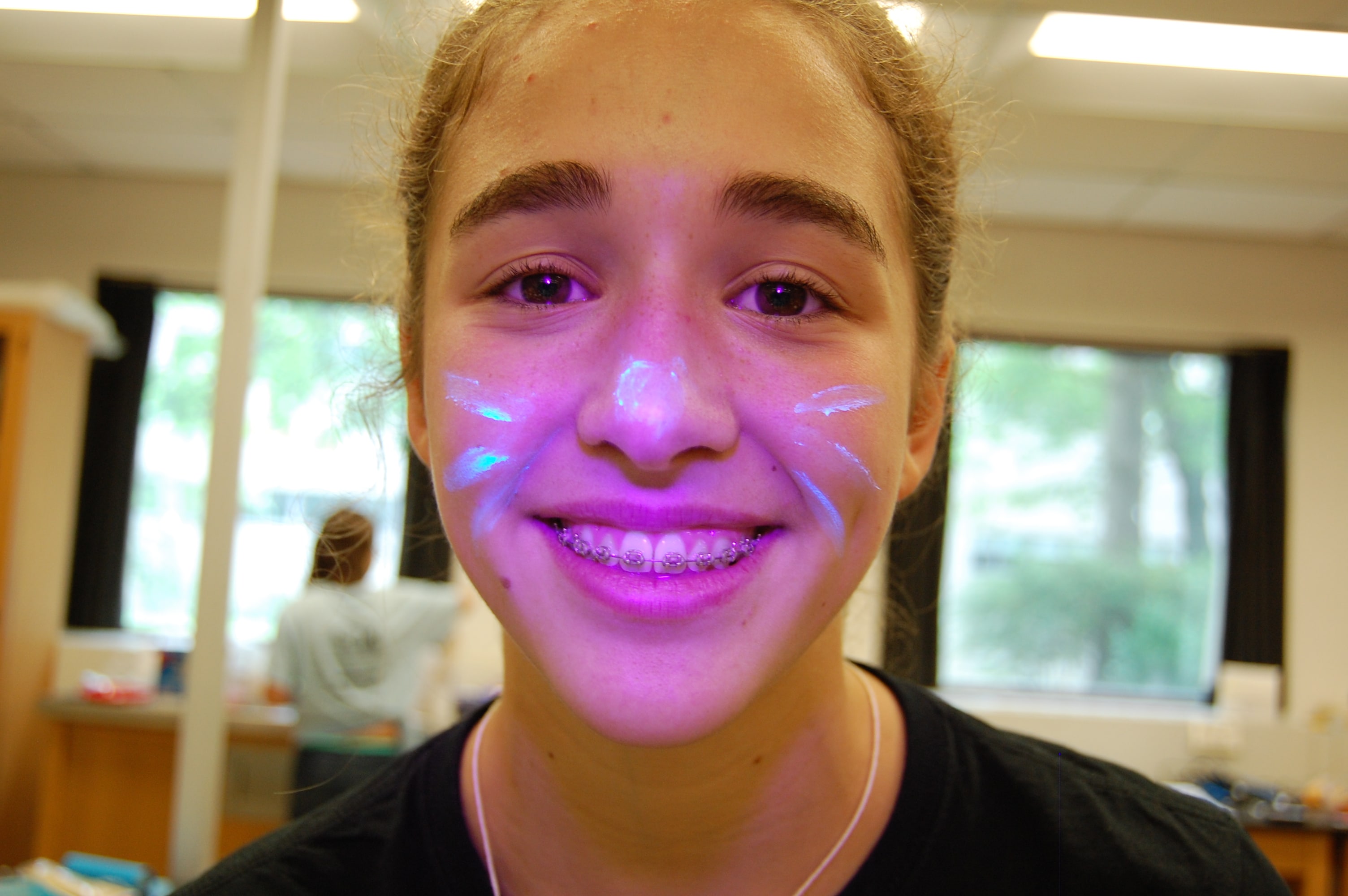 Close up of smiling young girl with pink glowing paint on her face.
