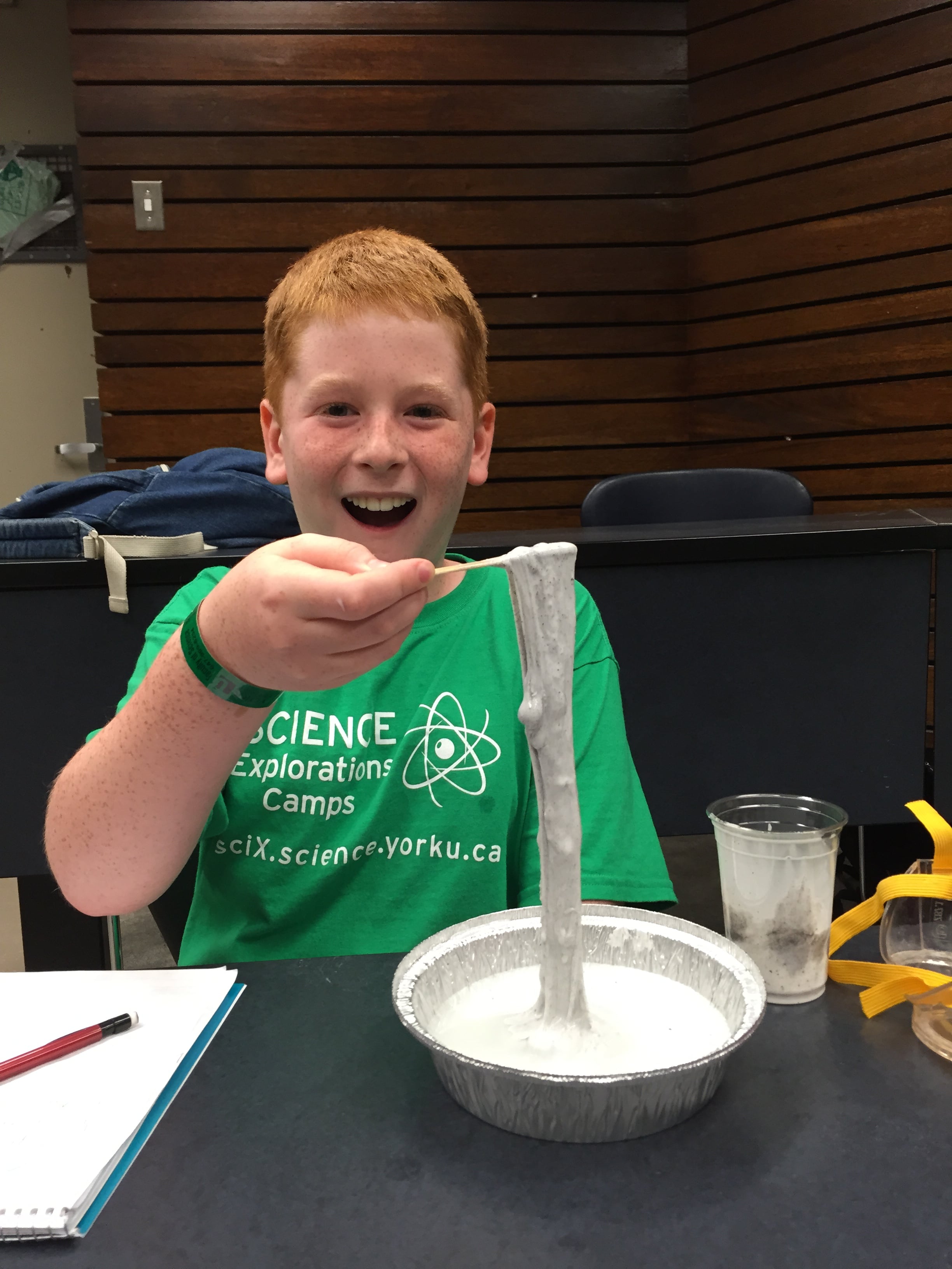 Young red headed boy holding grey liquid science experiment with excited expression.